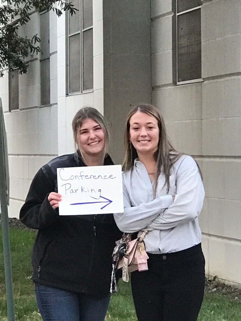 Two students holding a sign directing to the parking